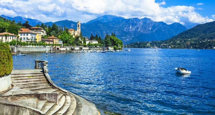 Clear blue waters of Lake Como bordered by elegant lakeside villas, church tower and alpine peaks in the background.