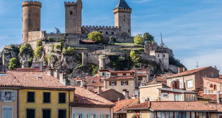 Burghügel Château de Foix, das über terrakottarot gedeckten Häusern an einem sonnigen Tag aufthront