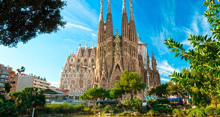 Basilika Sagrada Família mit komplizierten Türmen, die sich vor Grün und blauem Himmel erheben