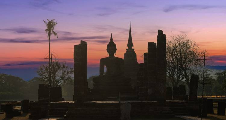 Silhouette d'un Bouddha assis et de stupas anciens à Sukhothai sur un ciel à l'aube aux couleurs éclatantes.