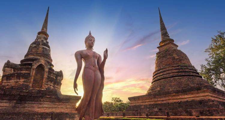 Bouddha debout gracieux flanqué de deux anciennes stupas en brique sous un ciel du soir coloré.