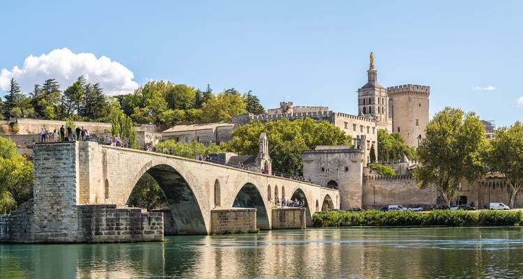 Le pont historique en pierre Pont Saint-Bénézet enjambant le Rhône avec des visiteurs marchant sur toute sa longueur par une journée ensoleillée.