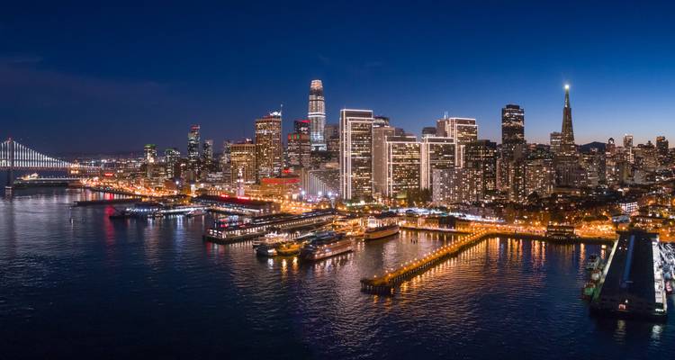 Panorama nocturne de la ligne d'horizon de San Francisco, des quais et des lumières du Bay Bridge se reflétant sur l'eau