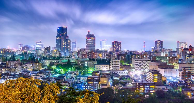 Nachtopname van de stad Sendai met glanzende wolkenkrabbers en long-exposure wolken boven een uitgestrekt stedelijk landschap.