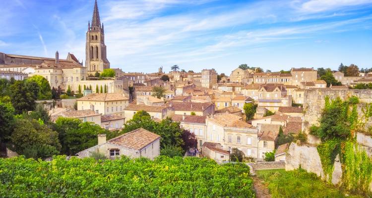 Rustikale Dächer und eine Kirchturmspitze ragen über das goldsteinerne Dorf Saint-Émilion inmitten von Weinbergen auf.
