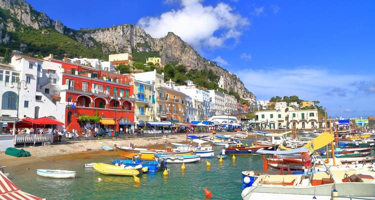 Puerto colorido de Capri lleno de botes, casas vibrantes y acantilados de piedra caliza dramáticos bajo un cielo brillante.