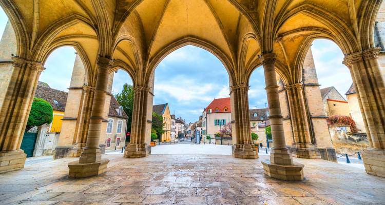 Arcade en pierre de style gothique donnant sur une place tranquille au coeur du centre historique de Beaune sous une lumière douce.