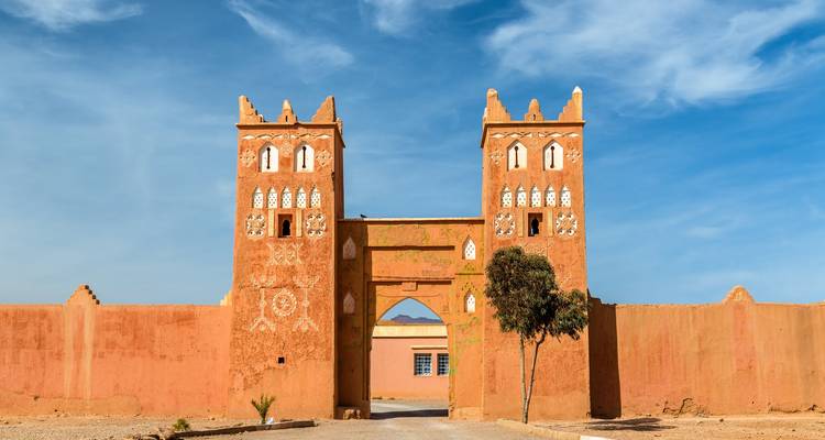 Klei-rode versterkte poort met twee vierkante torens versierd met traditionele Marokkaanse geometrische patronen tegen een blauwe lucht.