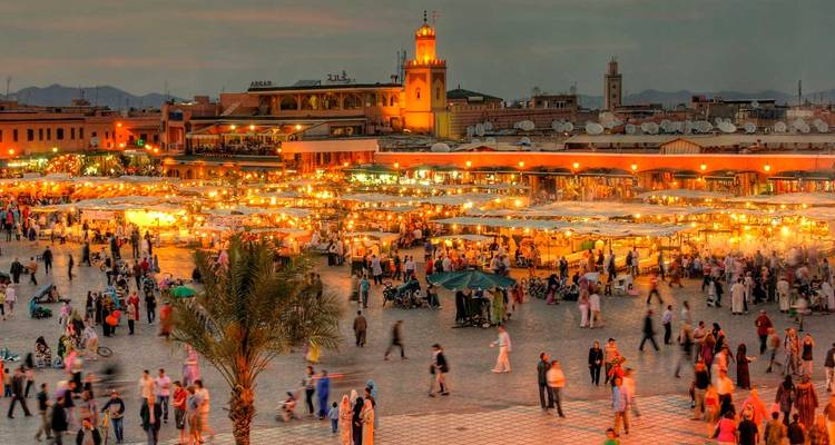 Drukke avondmarkt in Marrakesh die gloeit van honderden foodstalls, lichtjes en menigtes onder de schemering hemel.