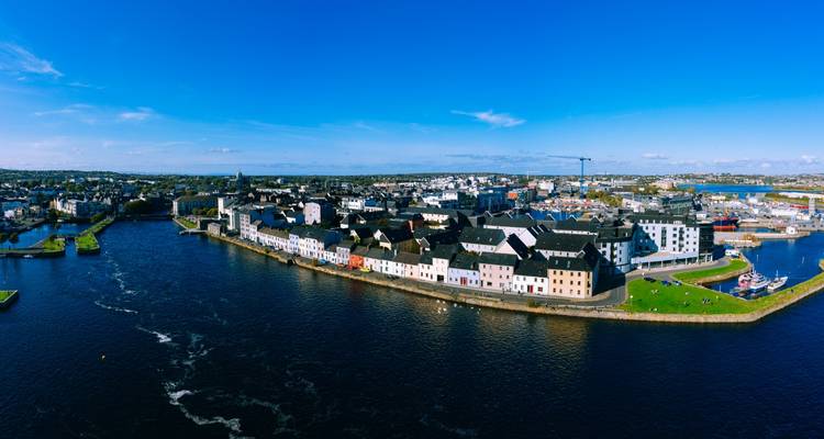 Luftaufnahme der farbenfrohen Häuser der Long Walk in Galway, die an der Flussmündung an einem klaren, sonnigen Tag aufgereiht sind.