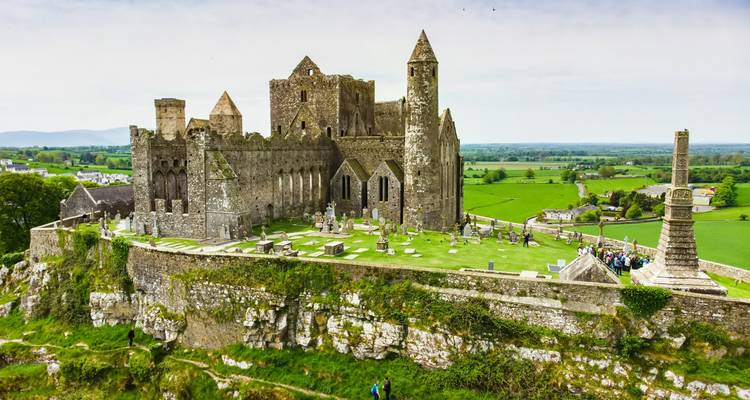 Historische Ruinen des Rock of Cashel auf einem Kalksteinvorsprung mit Besuchern, die den Friedhof erkunden.