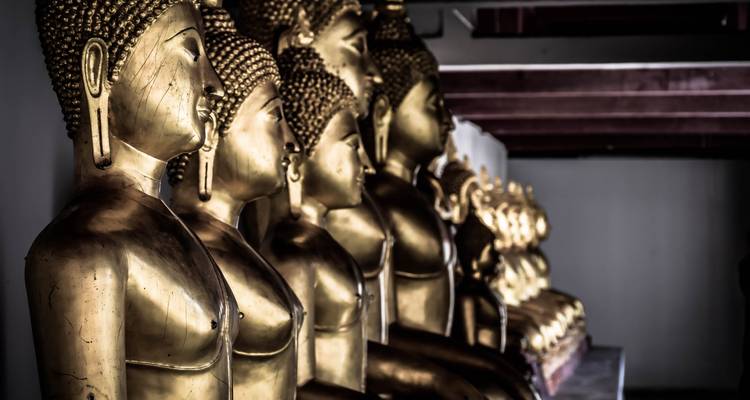 Rij van glanzende gouden Boeddha-beelden in het schemerige interieur van een Thaise tempel.