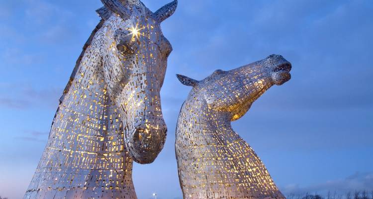 Deux sculptures géantes de têtes de chevaux en acier brillant, connues sous le nom de « The Kelpies », se dressent contre un ciel au crépuscule.
