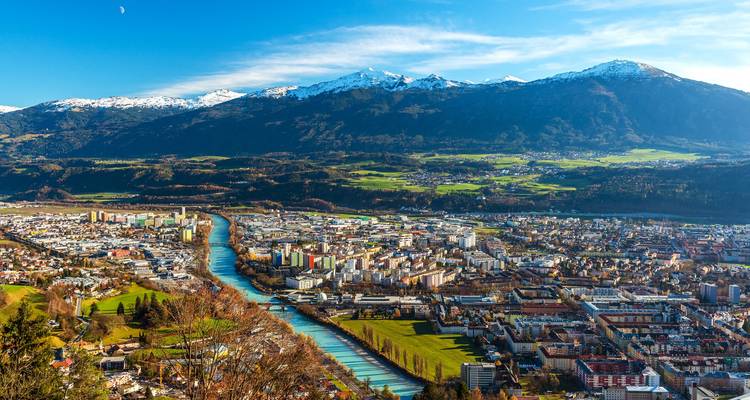 Panoramic aerial of Innsbruck with turquoise river winding through the valley below snow-capped Alps.