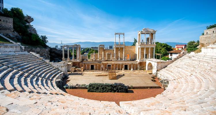 Antikes römisches Amphitheater mit Marmorsitzplätzen und säulengestützter Bühne vor klarem blauem Himmel