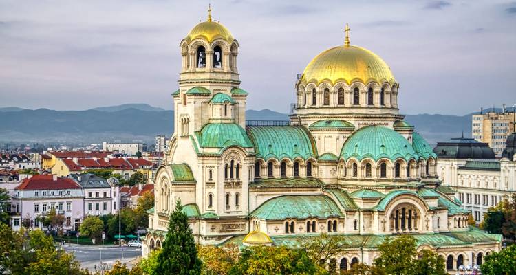 Nahaufnahme der grünen und goldenen Kuppeln der Alexander-Newski-Kathedrale vor nebligen Bergen