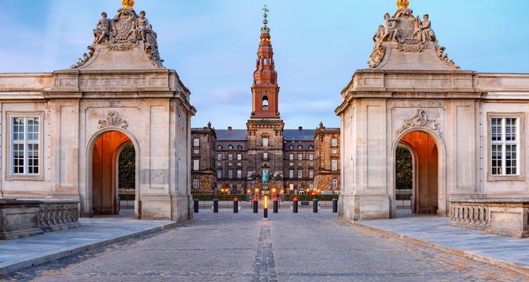 Des élégantes maisons de garde en pierre encadrant la vue vers le Palais de Christiansborg à Copenhague au crépuscule avec un ciel bleu doux.