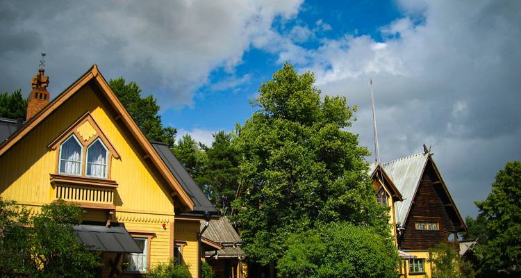 Charmantes maisons de campagne en bois entourées d'arbres feuillu sous un ciel bleu parsemé de nuages.
