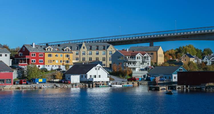 Des maisons en bois colorées le long de la façade maritime sous un long pont contre un ciel bleu profond dégagé à Kristiansund.