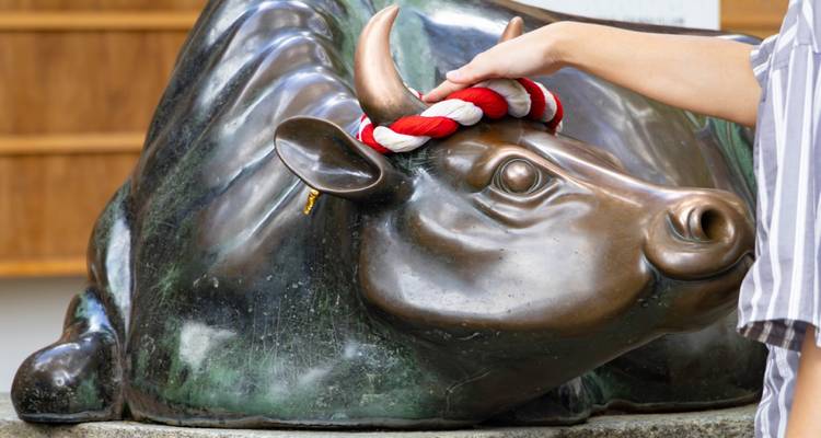 Een bezoeker raakt voorzichtig het bronzen koestandbeeld aan bij het Dazaifu Tenmangu-heiligdom.