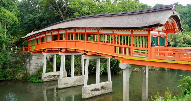 Een gebogen, vermiljoen houten brug die een rustige bosbeek in Japan overspant.