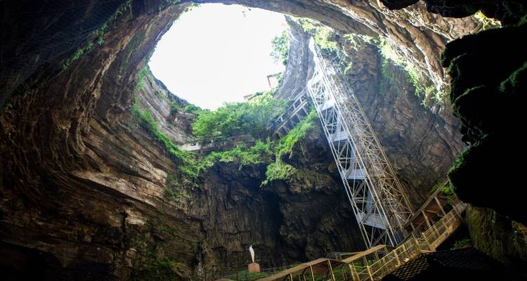 Gigantische vertikale Höhlenöffnung von Padirac mit Metalltreppe, die in den üppigen Abgrund hinabführt.