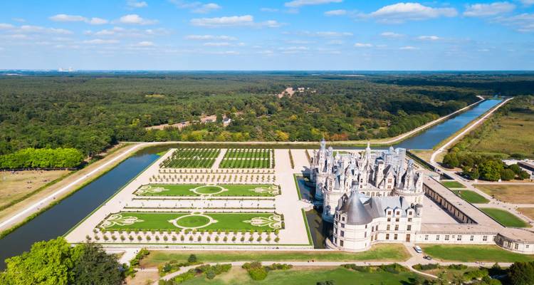 Luftaufnahme des Château de Chambord mit symmetrischen französischen Gärten und Kanälen, umgeben von Wald.