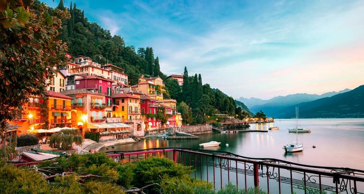 Les maisons colorées d'un village du Lac de Côme s'illuminant au crépuscule avec la baie calme et les montagnes environnantes.