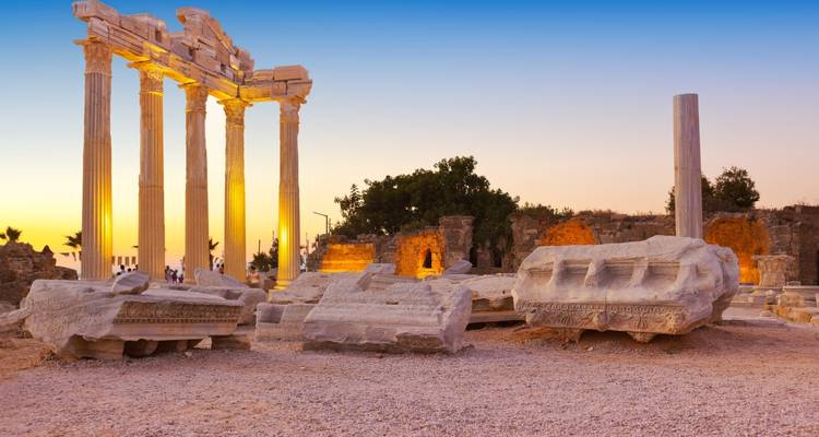 Le coucher de soleil doré baigne les colonnes debout et les blocs effondrés de l'ancien Temple d'Apollon au bord de la mer.