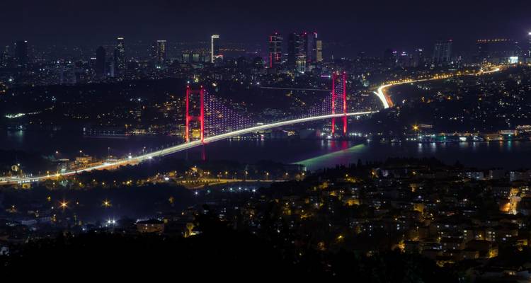 Panorama nocturne d'Istanbul avec le pont du Bosphore illuminé en rose vibrant enjambant les eaux scintillantes et les lumières de la ville.