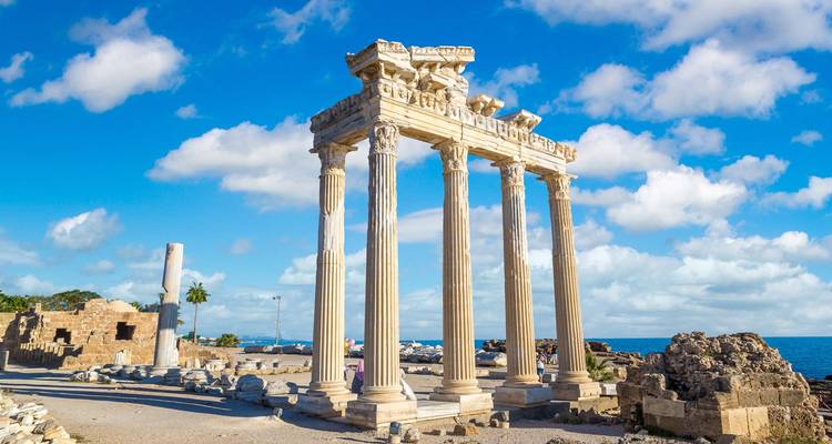 Well-preserved marble columns of the Temple of Apollo standing against a bright blue sky on the Mediterranean shore.