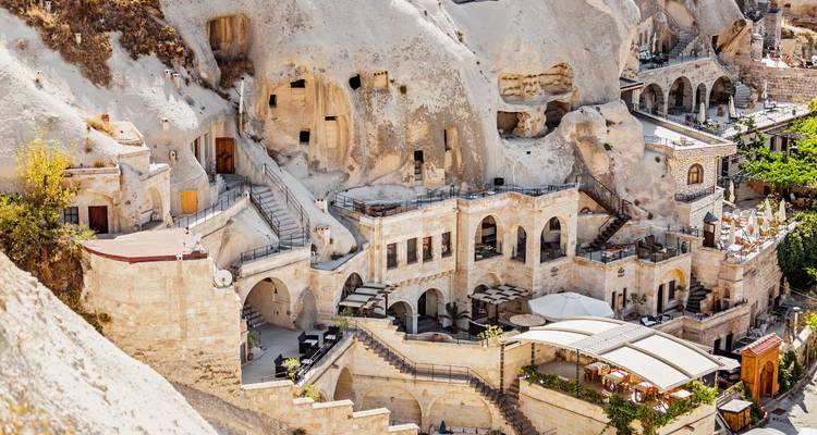 Terraced cave hotel complex carved into pale Cappadocia cliffs featuring arches and open-air dining areas.
