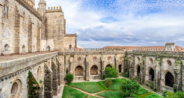 Cour de cloître historique avec galeries voûtées et espaces verts entretenus sous un ciel aux motifs.