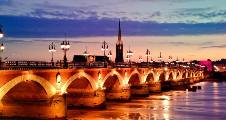 Le pont élégant Pont de Pierre à Bordeaux s'illumine au crépuscule, enjambant le fleuve Garonne sous un ciel coloré.