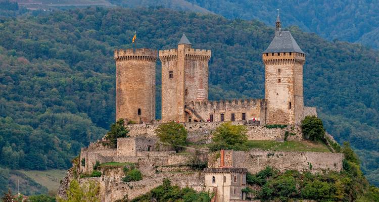 Le château de Foix, impressionnant château médiéval perché sur une colline rocheuse surplombant une forêt dense.