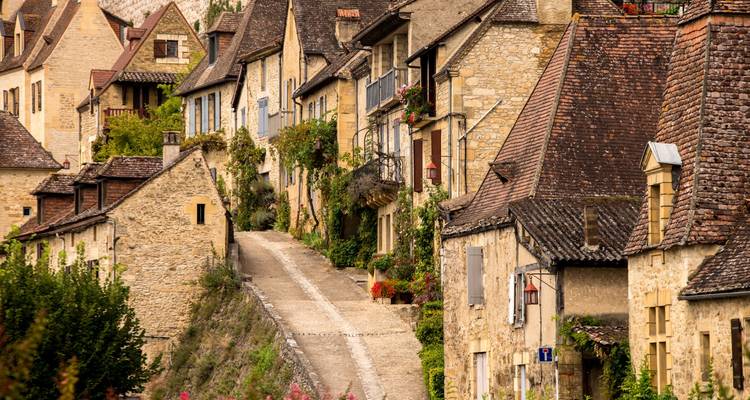 Rue pittoresque d'un charmant village médiéval en pierre bordée de maisons rustiques et de verdure.
