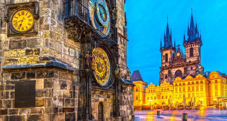 Vue rapprochée de l'Horloge astronomique de Prague avec la Place de la Vieille Ville illuminée et l'Église Týn à l'heure bleue.