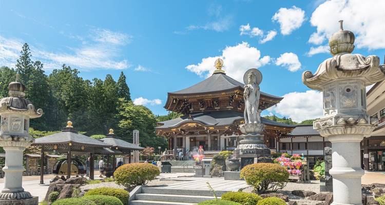 Complexe de temple japonais traditionnel avec des lanternes en pierre et des arbustes entretenus sous un ciel bleu.