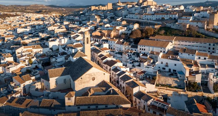Pueblo andaluz en ladera con casas blancas y un castillo en la cima de la colina bañado por la cálida luz de la tarde.