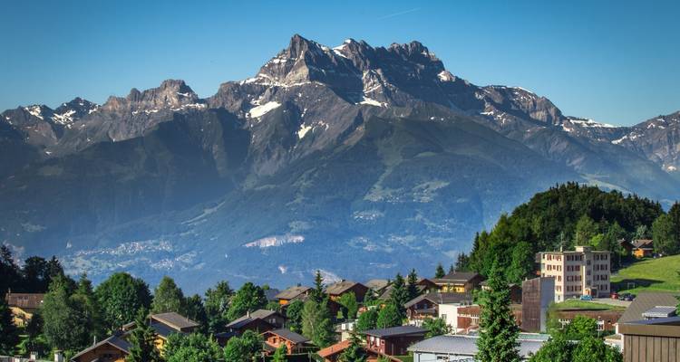 Pueblo alpino salpicado de chalets bajo un pico nevado dramatico en un claro día de verano.
