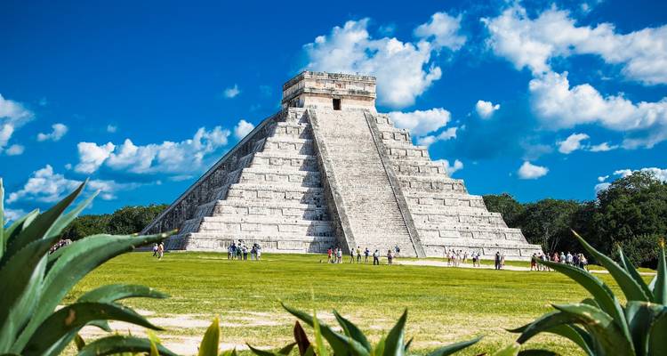 Die aufragende Kalksteinpyramide El Castillo erhebt sich vom grasigen Platz in Chichén Itzá unter einem leuchtend blauen Himmel.