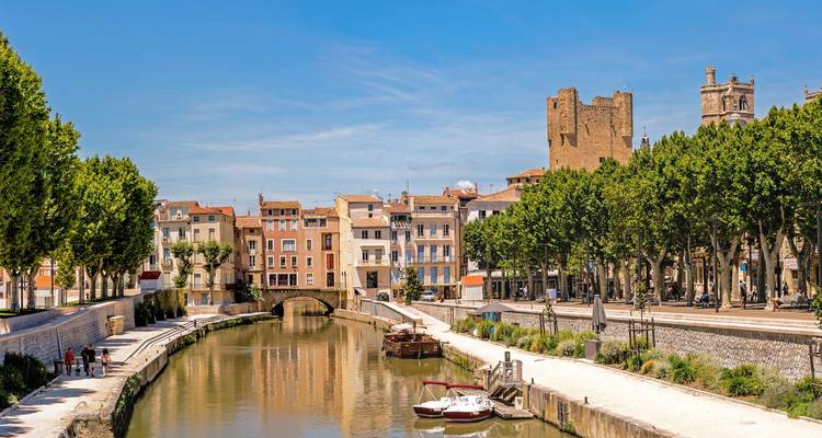 Calm canal lined with pastel houses and shaded by plane trees in sun-drenched Narbonne