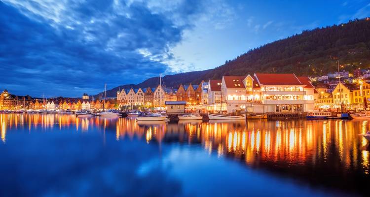 Vue nocturne du quai Bryggen de Bergen avec des maisons en bois colorées se reflétant dans les eaux calmes du port.