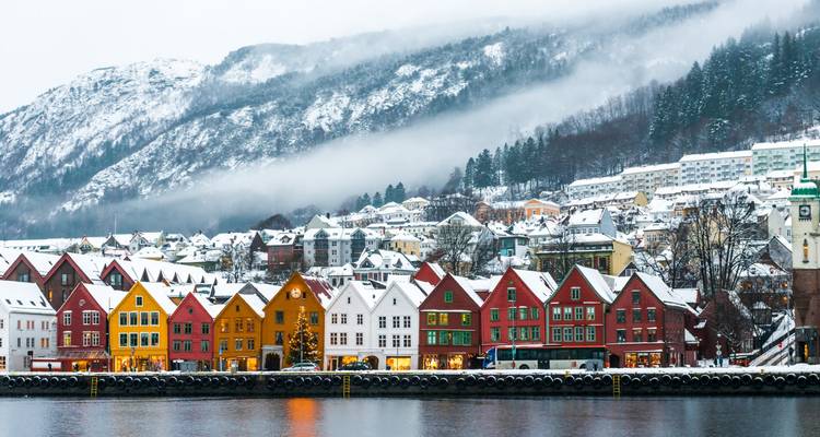 Les maisons enneigées de Bryggen à Bergen se reflétant dans le port avec les montagnes brumeuses en arrière-plan.