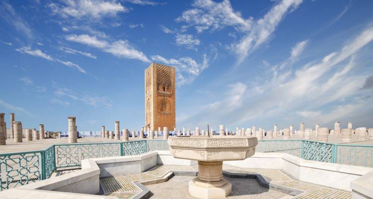 Fontaine en pierre et rangées de colonnes menant à la Tour Hassan à Rabat sous un ciel bleu éclatant.