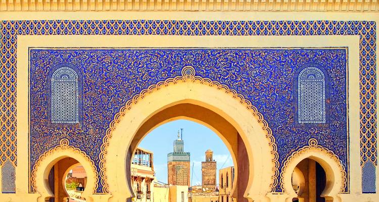 La porte Bab Bou Jeloud aux carreaux bleu vibrant à Fès, avec une vue à travers l'arche sur les minarets et la médina au-delà.