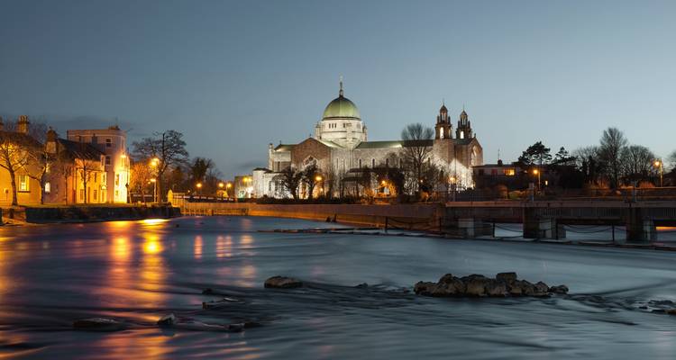 La Cathédrale de Galway illuminée au crépuscule se reflétant sur les eaux calmes de la rivière