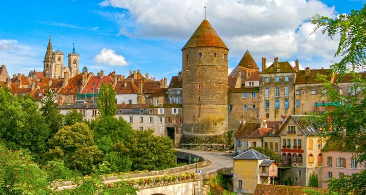Charmante mittelalterliche Stadtlandschaft von Semur-en-Auxois mit zylindrischem Turm, Steinhäusern und üppiger Vegetation unter blauem Himmel.