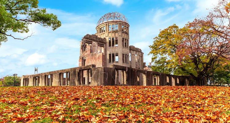 Le Dôme de la Bombe Atomique encadré par des feuilles d'automne aux couleurs éclatantes sous un ciel bleu brillant.