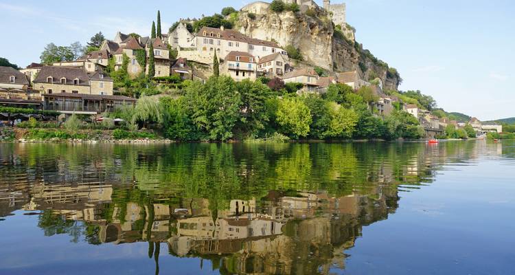Village pittoresque au bord de la rivière s'accrochant à une falaise, se reflétant parfaitement sur une eau calme.